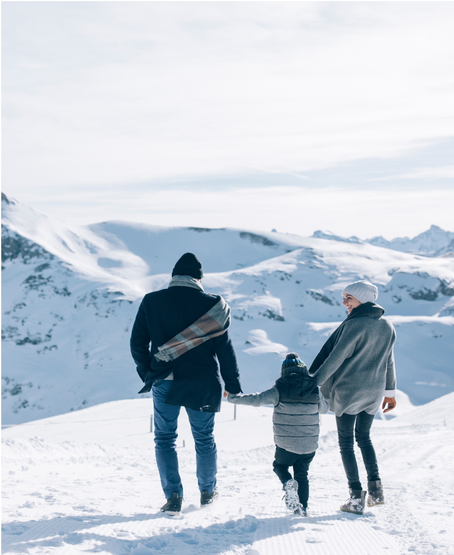Ein Vater und eine Mutter halten Händchen mit ihrem Kind am verschneiten Berghang.