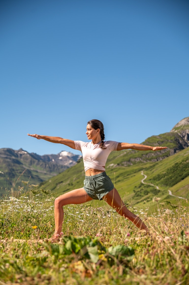 Eine Yoga-Frau posiert inmitten wild-wachsenden Sommerblumen.