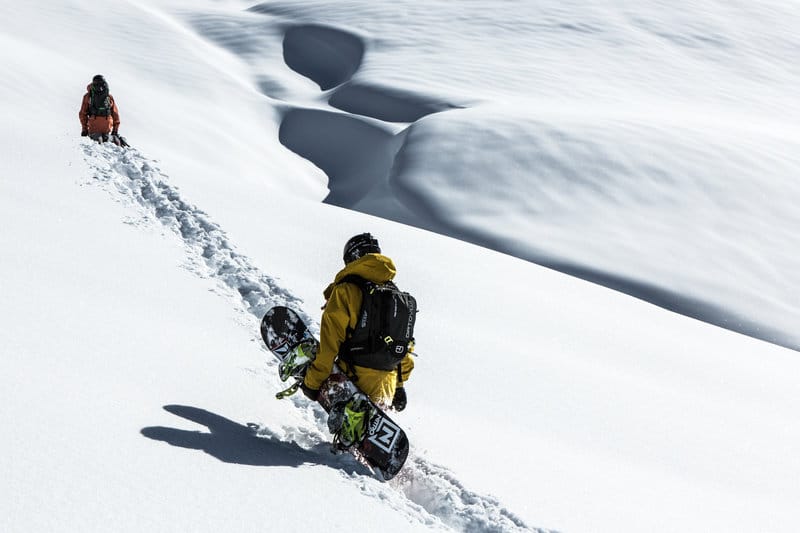 Ein Snowboarder mit Snowboard in der Hand spurt eine Spur durch den tiefen Neuschnee.